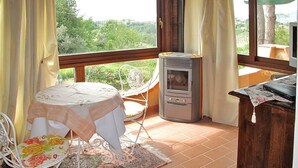 Un balcón con mesa y sillas, una estufa de leña y vistas a la vegetación.