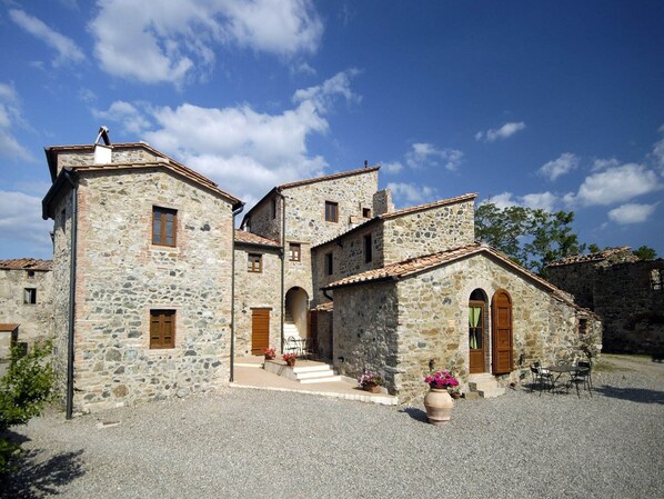A stone building with multiple levels and arched doorways, surrounded by gravel.