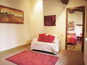 A room with a white sofa, red cushions, a red rug, and a painting of a landscape.
