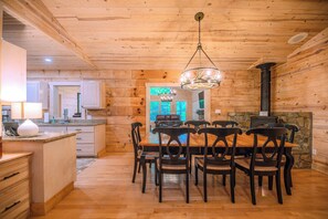 Cozy cabin-style room with a dining table, kitchen area, and stone fireplace.
