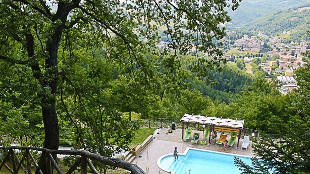 Ein Poolbereich mit einer Laube, umgeben von Bäumen und Blick auf eine Stadt im Hintergrund.