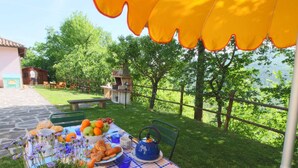 Ein Essbereich im Freien mit Tisch, gedeckt für eine Mahlzeit, umgeben von Grünpflanzen und Blick auf die Landschaft.