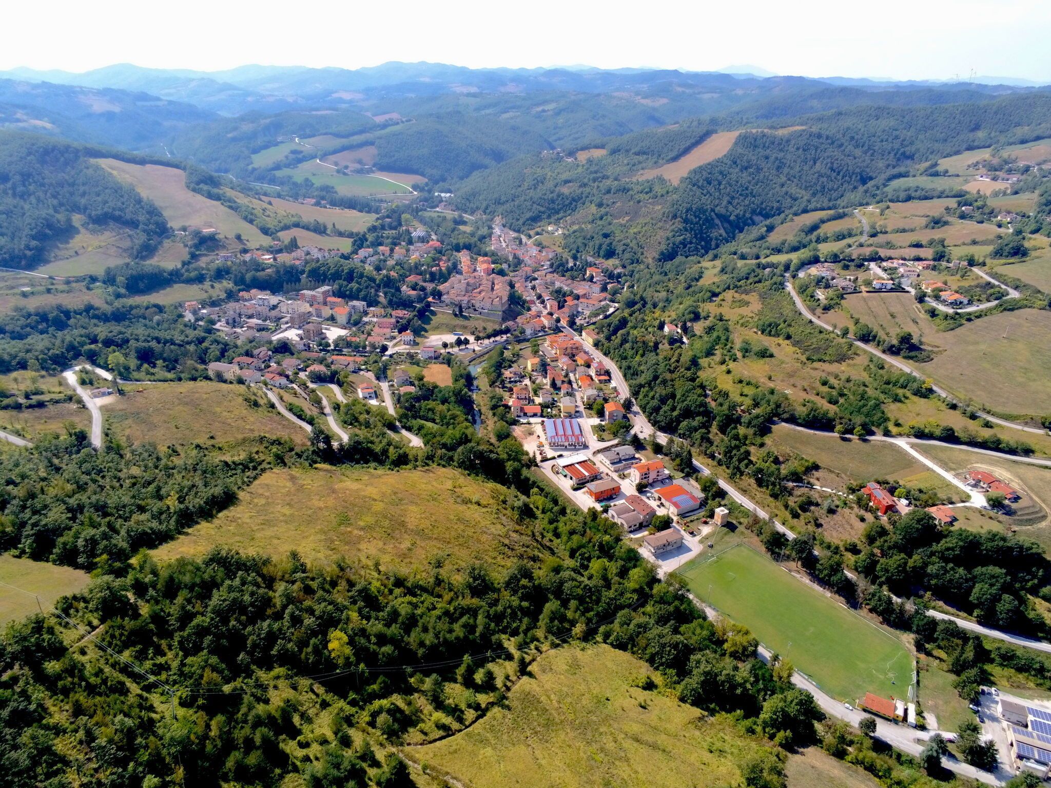 Eine Vogelperspektive auf eine Stadt mit einem zentralen Platz, umgeben von Wohngebäuden und grünen Feldern.
