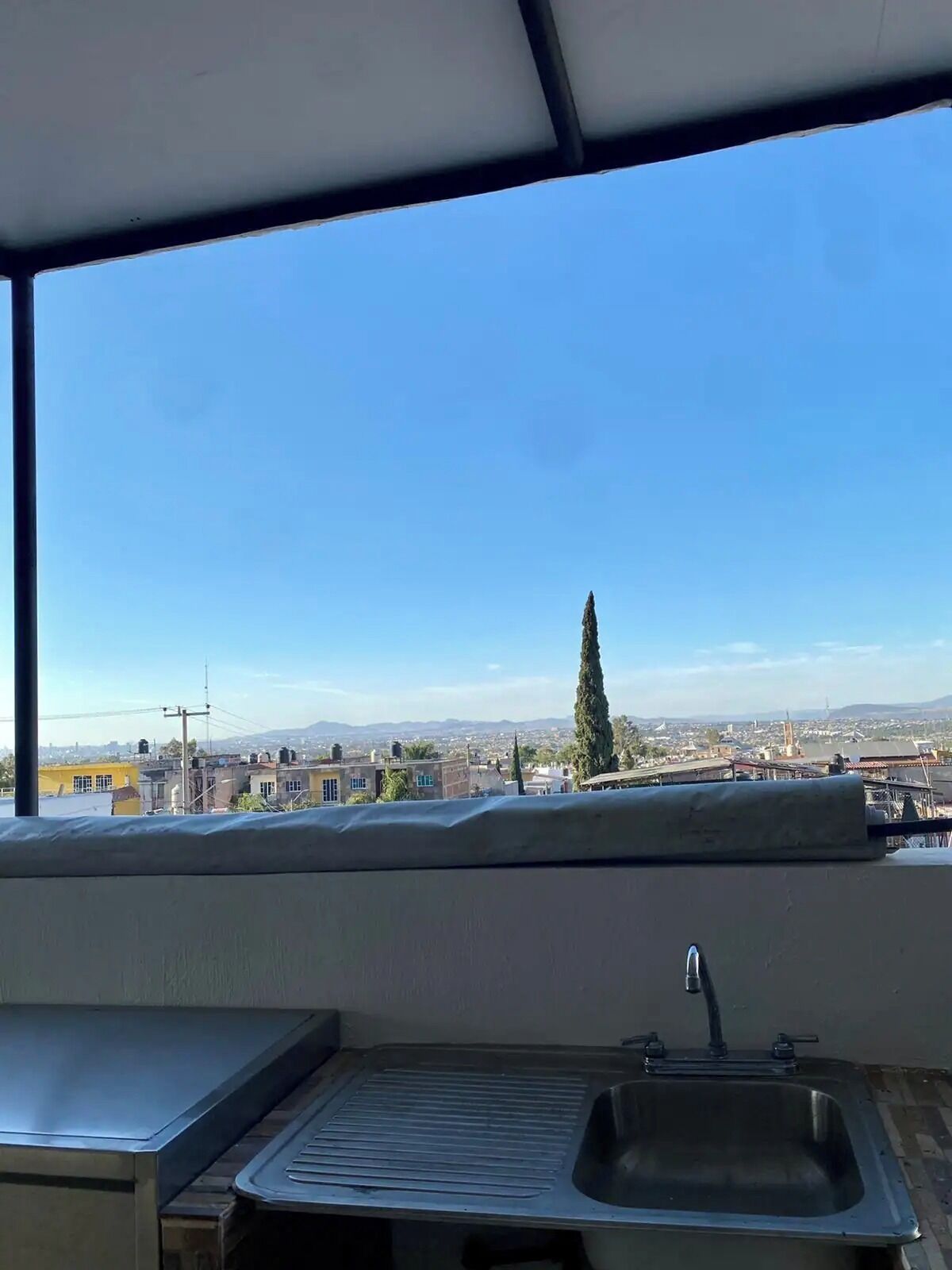 Una cocina con un ventanal grande, un lavamanos y vistas a un paisaje urbano.