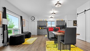 Een moderne keuken met grijze kastjes, een eettafel met stoelen en een groot raam met gordijnen.