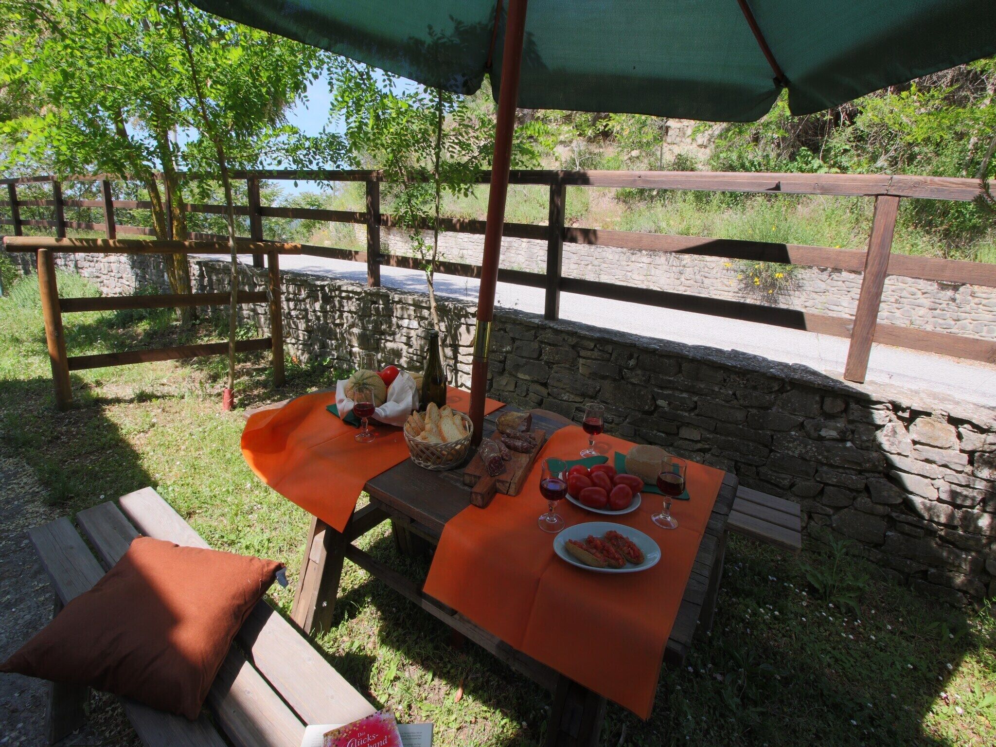 Un espace de restauration en plein air, avec un mur en pierre en arrière-plan, des meubles en bois et une table dressée avec de la nourriture et des boissons.