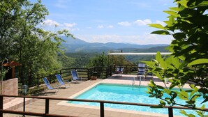 A swimming pool with a view of mountains, surrounded by a wooden deck and blue chairs. - Farmhouse in Apecchio with Pool & Spa (Apecchio)
