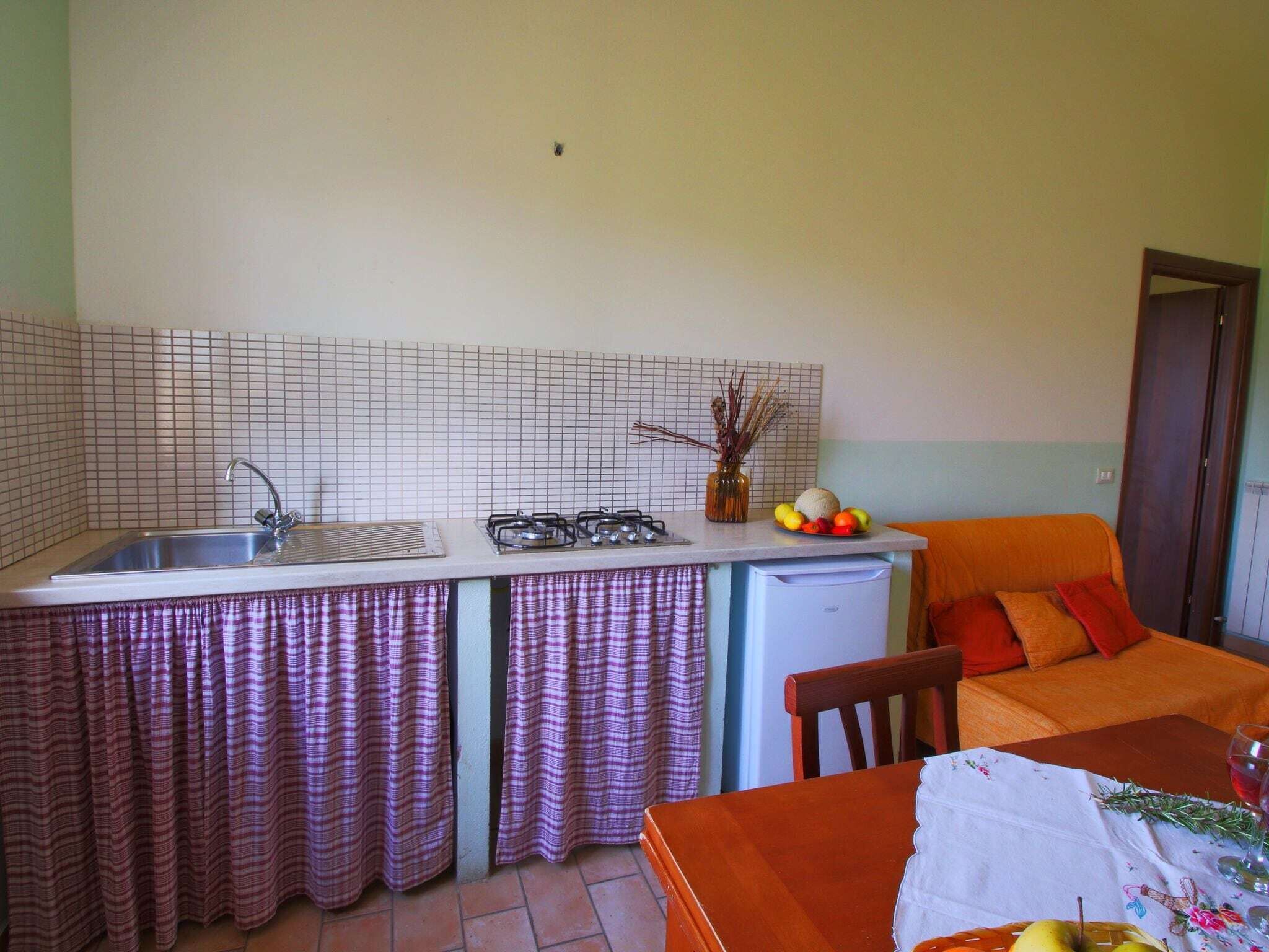 Une cuisine compacte équipée d’un évier, d’une cuisinière et d’un réfrigérateur, une table à manger avec un set de table, et un canapé dans l’espace de vie adjacent.