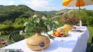 A table set outdoors with a view of green hills, a wooden vase with flowers, a fruit plate, and a wine glass. - Mansion in Apecchio with Pool (Apecchio)