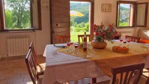 A dining area with a table set for four, a vase of flowers, and a view of the outdoors. - Mansion in Apecchio with Pool (Apecchio)