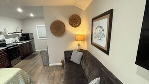 A compact living space with a kitchenette, a sofa, a bedside table, and a framed picture on the wall.