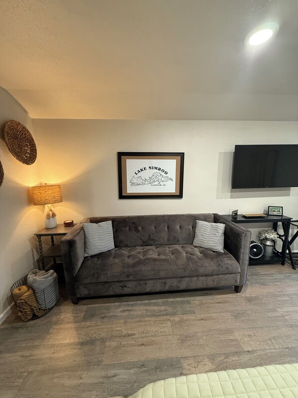 A living room with a grey sofa, a framed picture on the wall, a lamp, and a television.