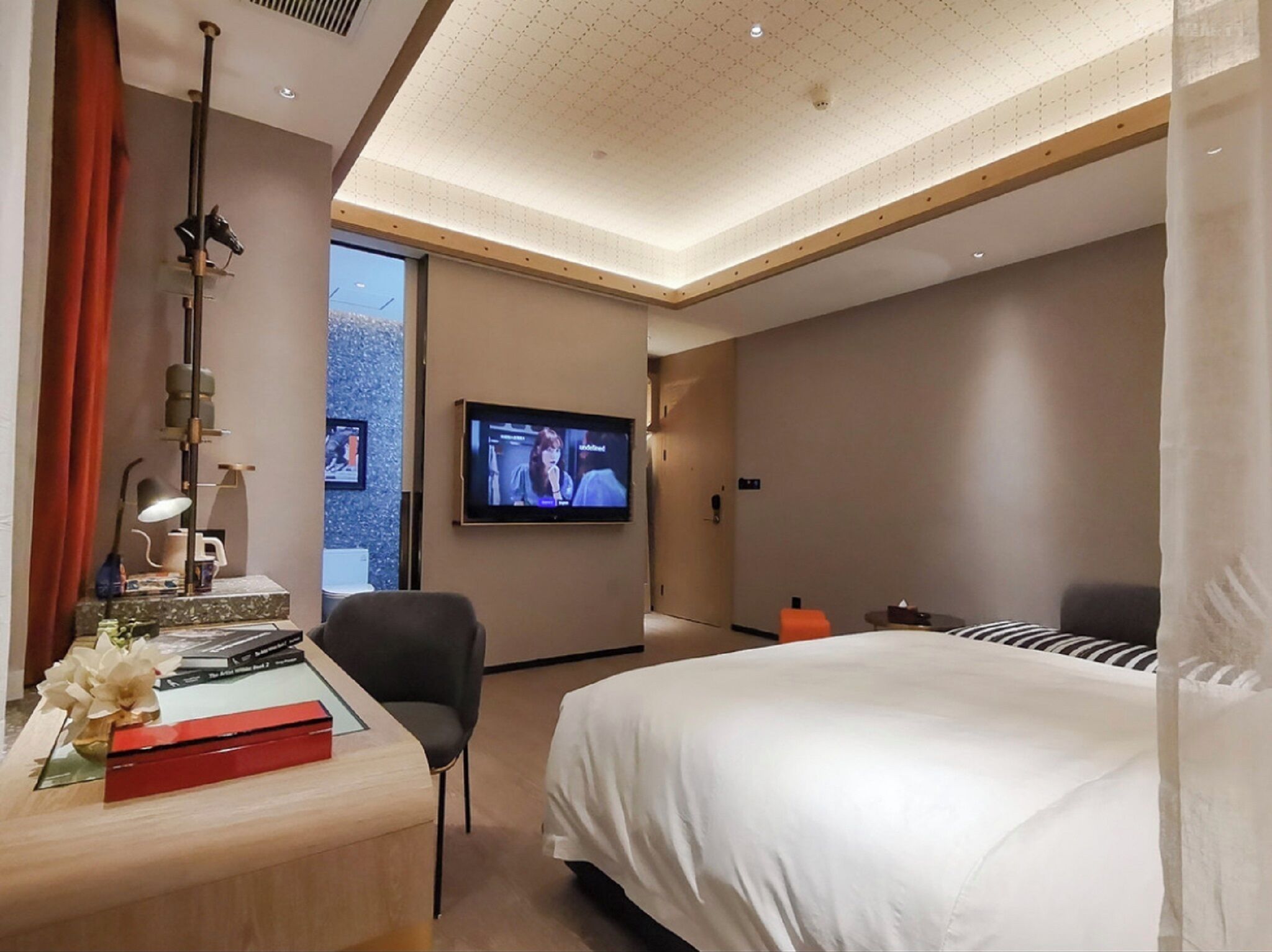 Ein modernes Hotelzimmer mit Bett, Schreibtisch mit Lampe, Fernseher und Blick ins Freie.