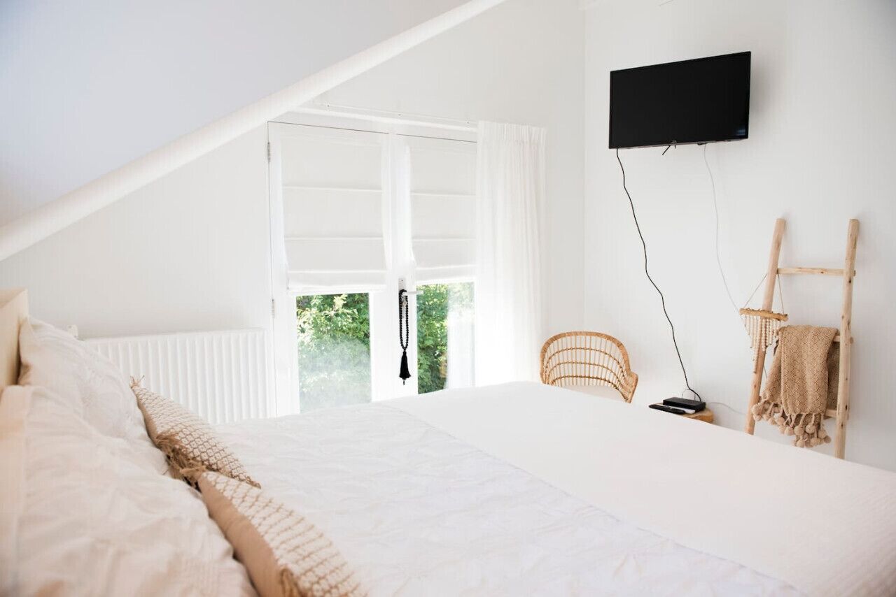 A bedroom with a large bed, a television mounted on the wall, a window with curtains, and a wooden chair.