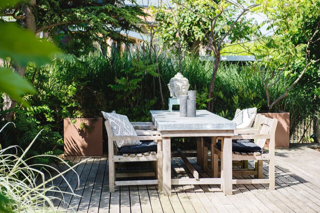 An outdoor wooden deck with a table and chairs, surrounded by lush greenery.