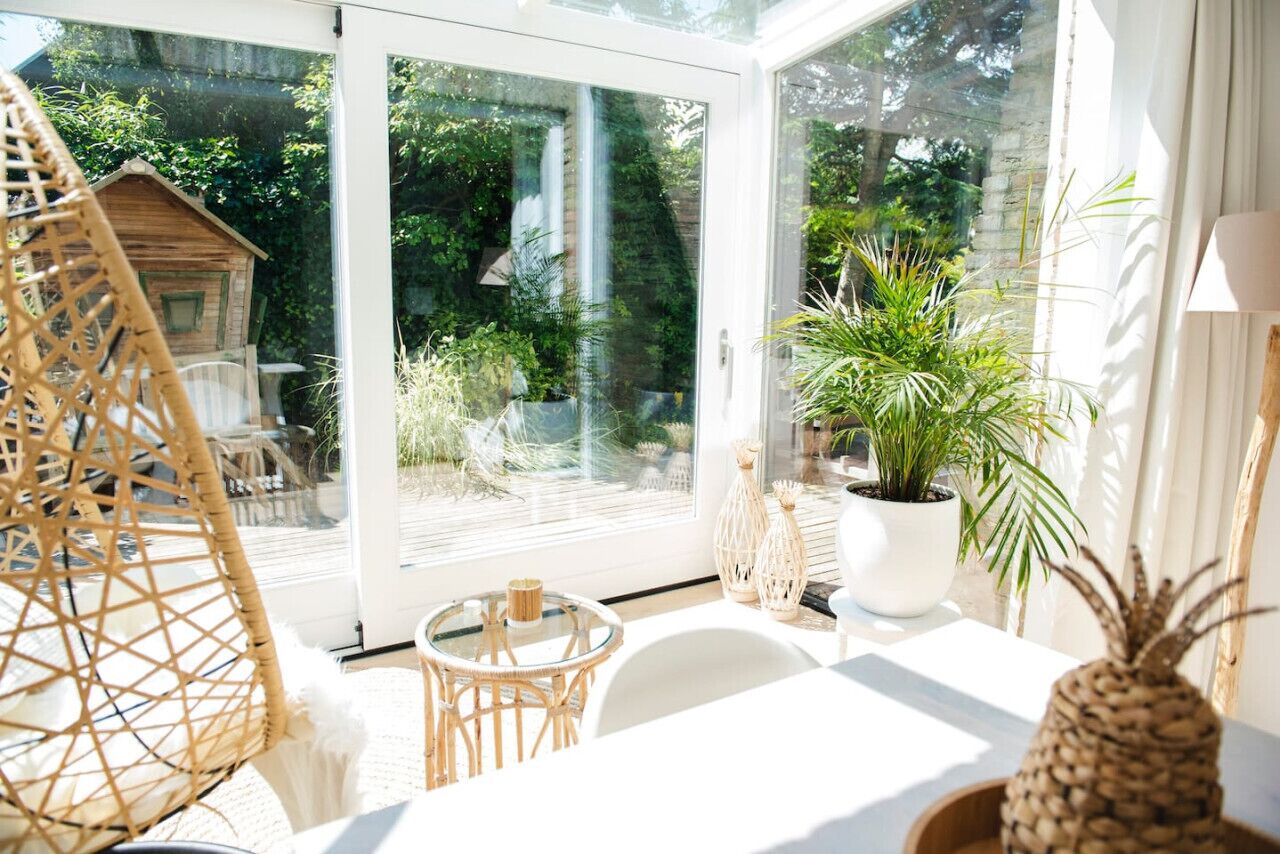 A bright room with a glass door leading to a garden, wicker furniture, and potted plants.