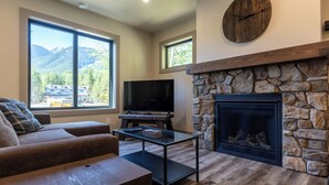 A living room with a stone fireplace, a television, and a large window offering a mountain view. - Newly Built 2 Bedrooms. Sleeps 4 Adults. AC (Fernie)
