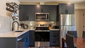 A modern kitchen with dark cabinets, stainless steel appliances, and a wooden dining table. - Newly Built 2 Bedrooms. Sleeps 4 Adults. AC (Fernie)