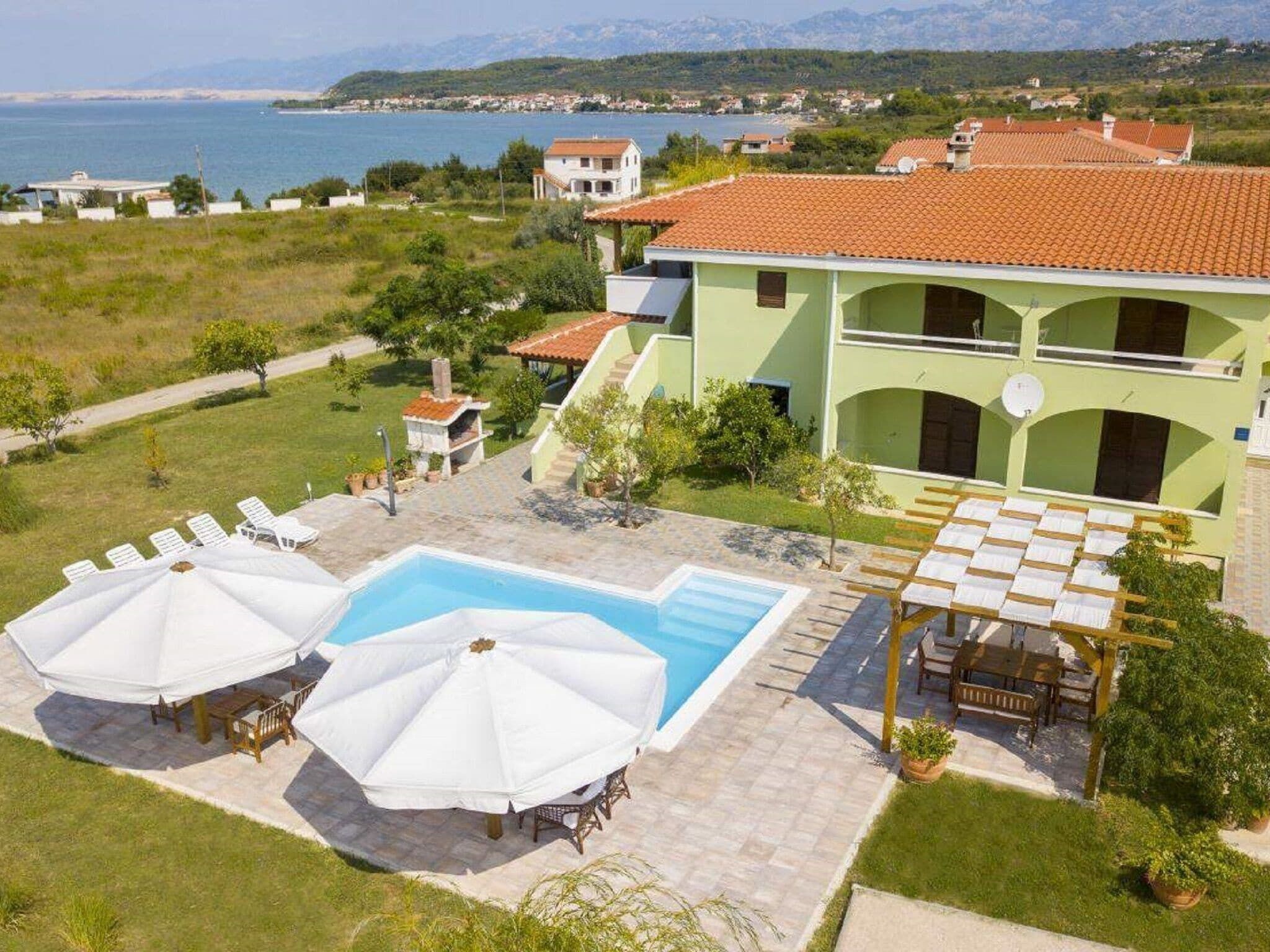 A pool area with umbrellas, a covered seating area, and a view of the sea and mountains.