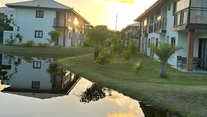 A residential area with modern houses, a calm water body reflecting the buildings, and a clear sky.