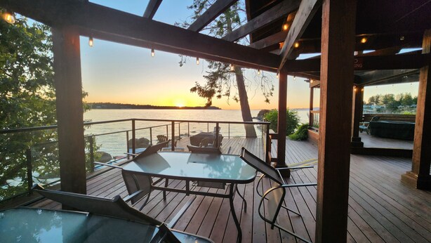 Terraza de madera con asientos al aire libre, con vista a un cuerpo de agua durante el atardecer.