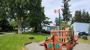 Un parque infantil con una estructura de juego temática de barco, una bandera y un coche estacionado cerca.