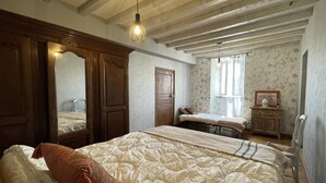 Een slaapkamer met een groot bed, een kleiner bed, een kaptafel, een spiegel en een raam met bloemenbehang.