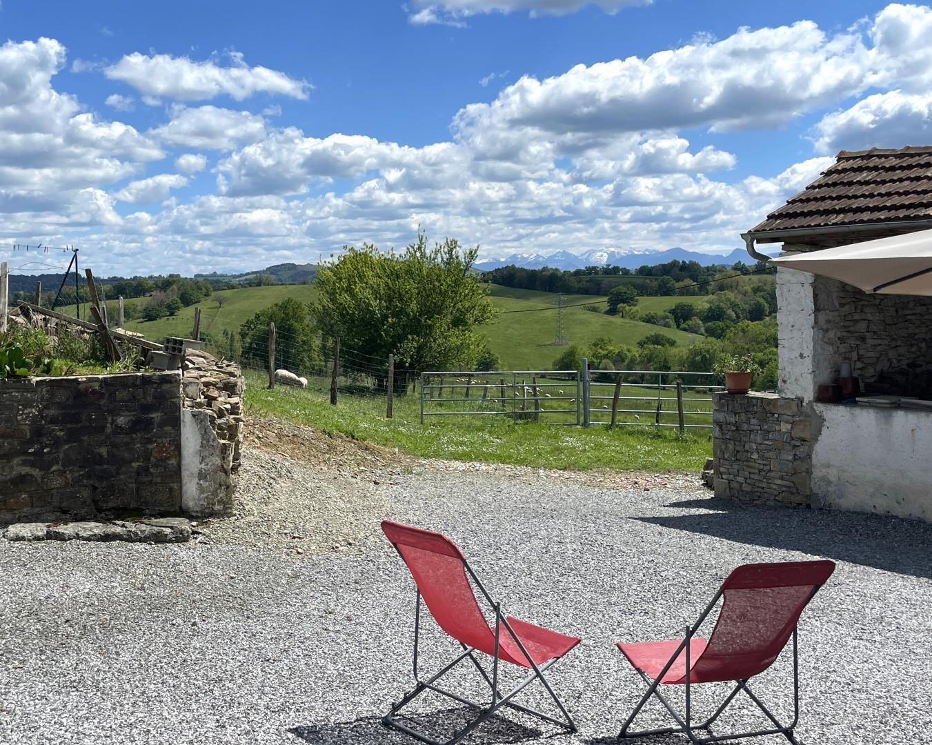 A gravel patio with two red chairs facing a scenic view of green hills and a clear sky.