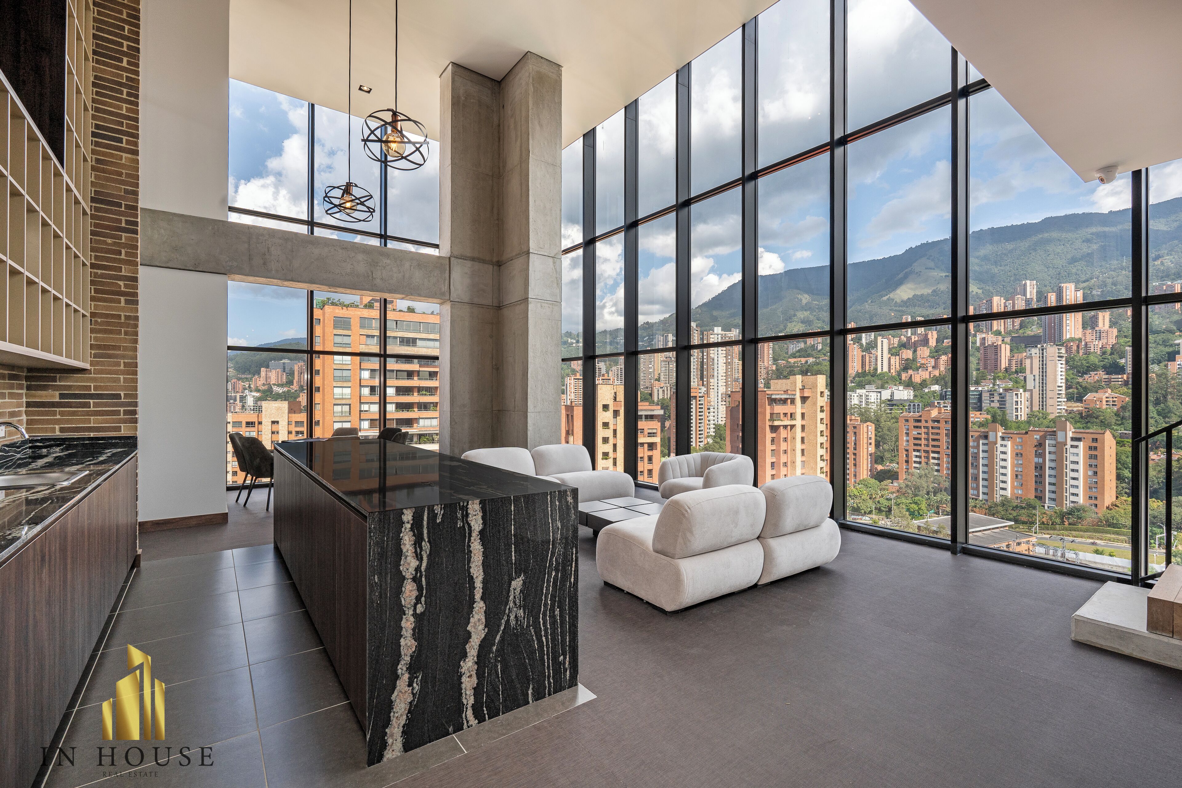 Una cocina moderna con una isla de mármol, un área de comedor con sofás blancos y ventanas amplias con vistas a la ciudad.