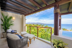 Enjoy the serene ocean views from this expansive balcony, featuring a seating area and lush tropical surroundings.