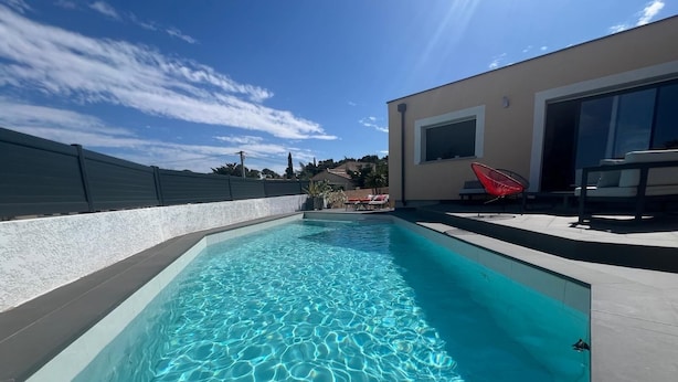 Une piscine rectangulaire à l’eau d’un bleu limpide, entourée d’un mur blanc et d’une clôture sombre.