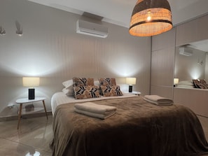 Une chambre moderne avec un grand lit, deux tables de chevet avec des lampes, un miroir et un appareil de climatisation.