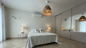 Une chambre moderne avec un grand lit, des lampes de chevet, un luminaire suspendu, un grand miroir et un appareil de climatisation.