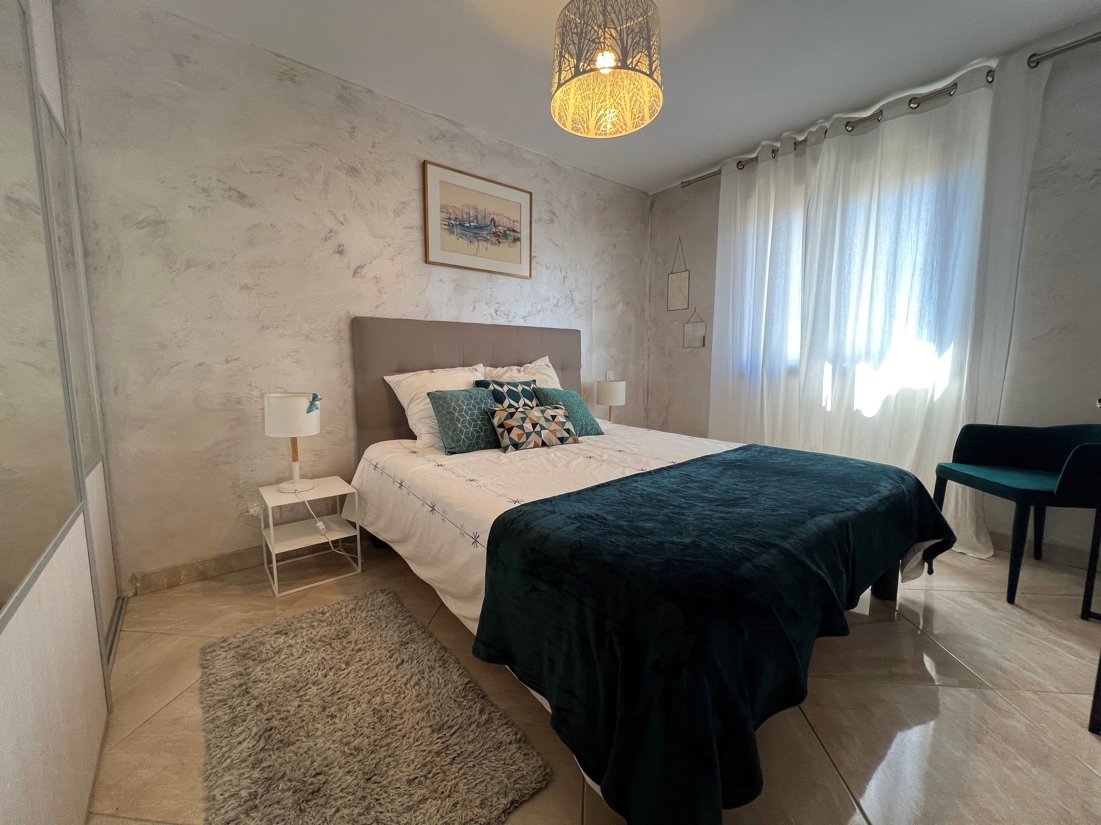Een slaapkamer met een bed, nachtkastjes, een vloerkleed, een stoel en een hanglamp.