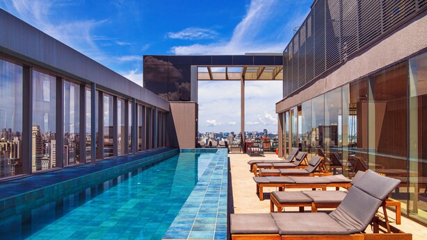 A rooftop infinity pool with lounge chairs, large windows, and a city view. - Movinn Nine - Jardim Paulista (São Paulo)