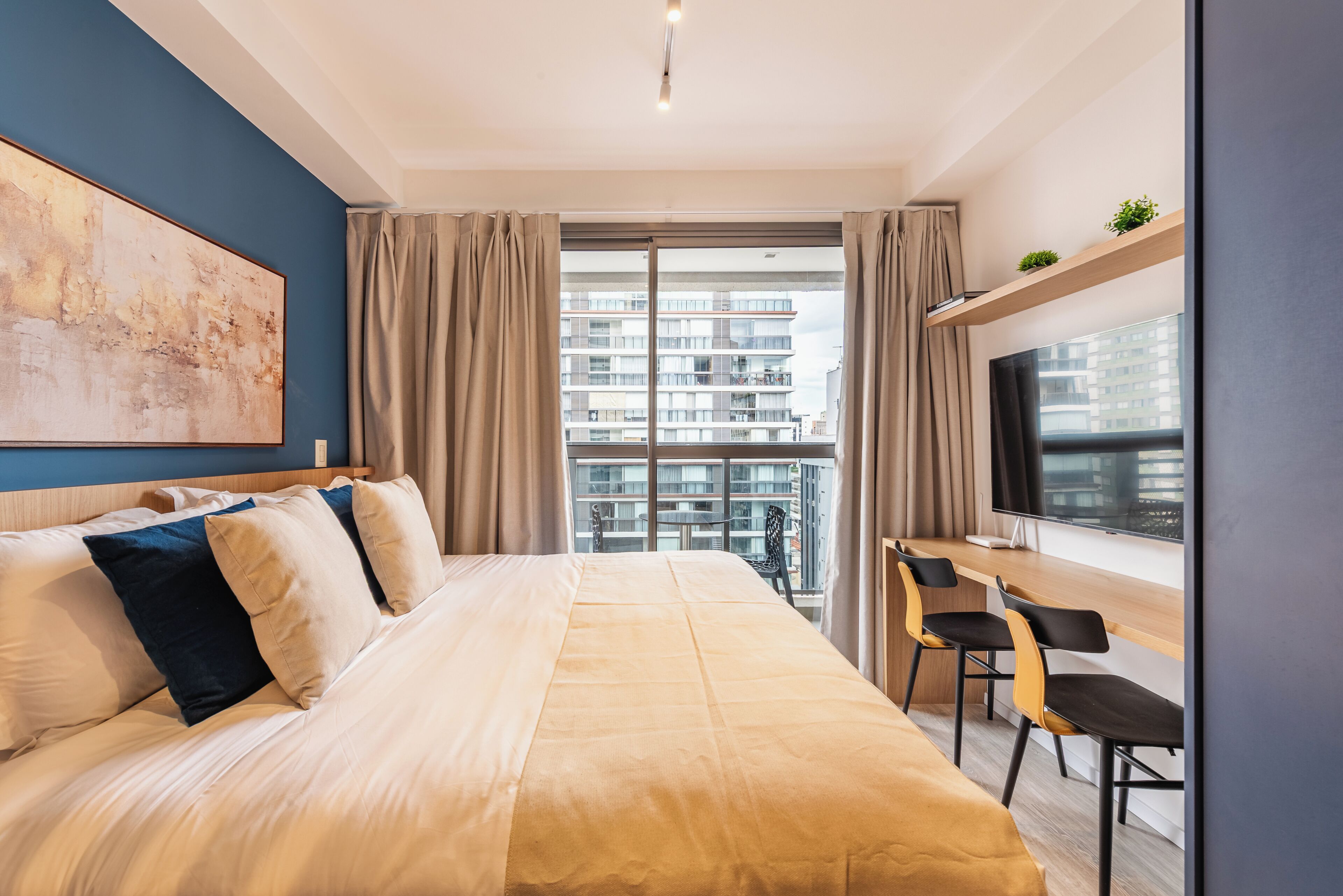 Ein modernes Hotelzimmer mit einem großen Bett, einem Schreibtisch mit Stühlen, einem Fernseher und einem Balkon mit Blick auf die Stadt.