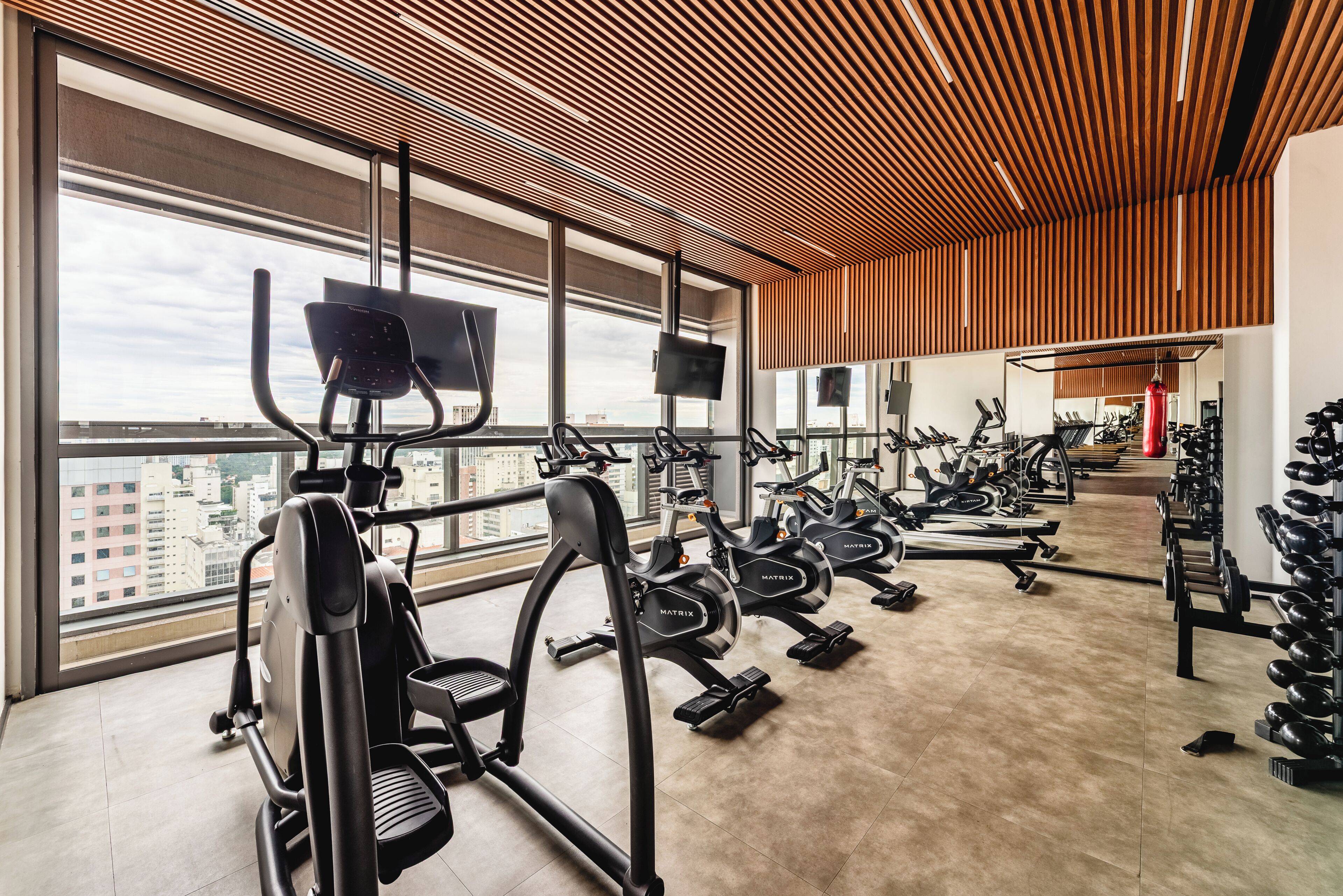 Une salle de sport équipée de machines de cardio, de bancs de musculation et dotée d’une grande fenêtre offrant une vue sur la ville.