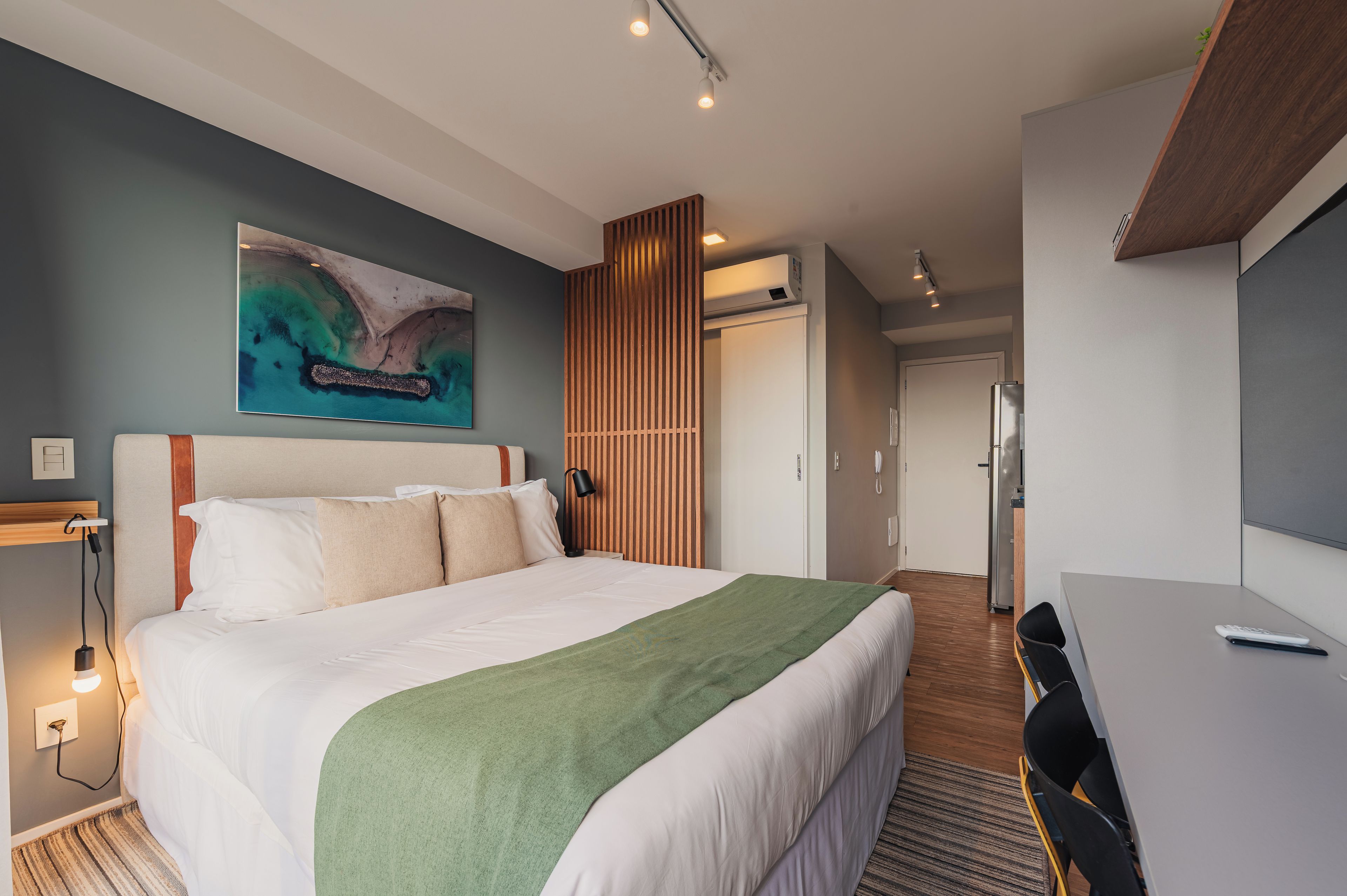 A hotel room with a large bed, a desk, a television, and a painting on the wall.