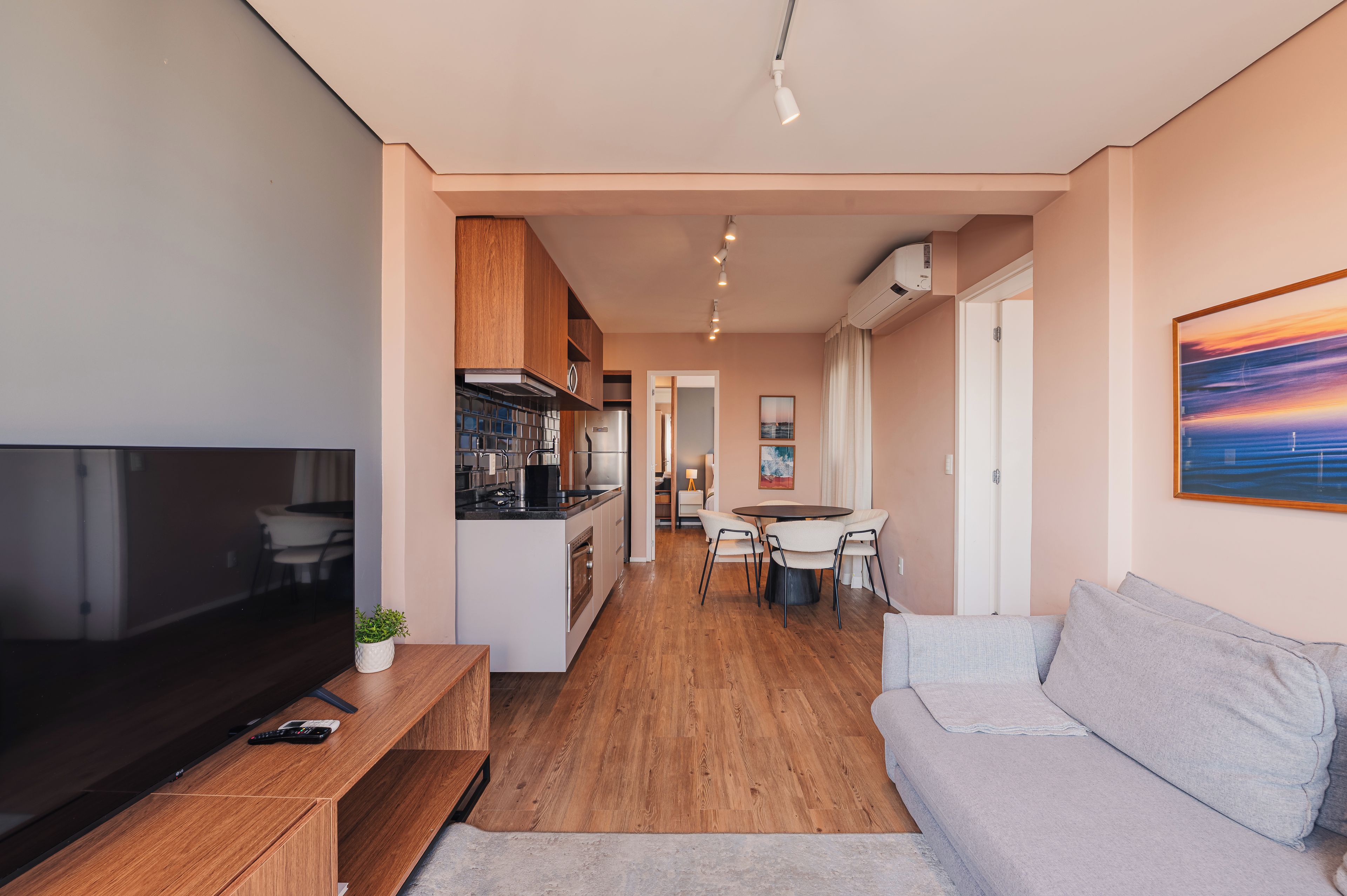 A modern apartment with a TV, wooden furniture, a dining area, and a kitchen.