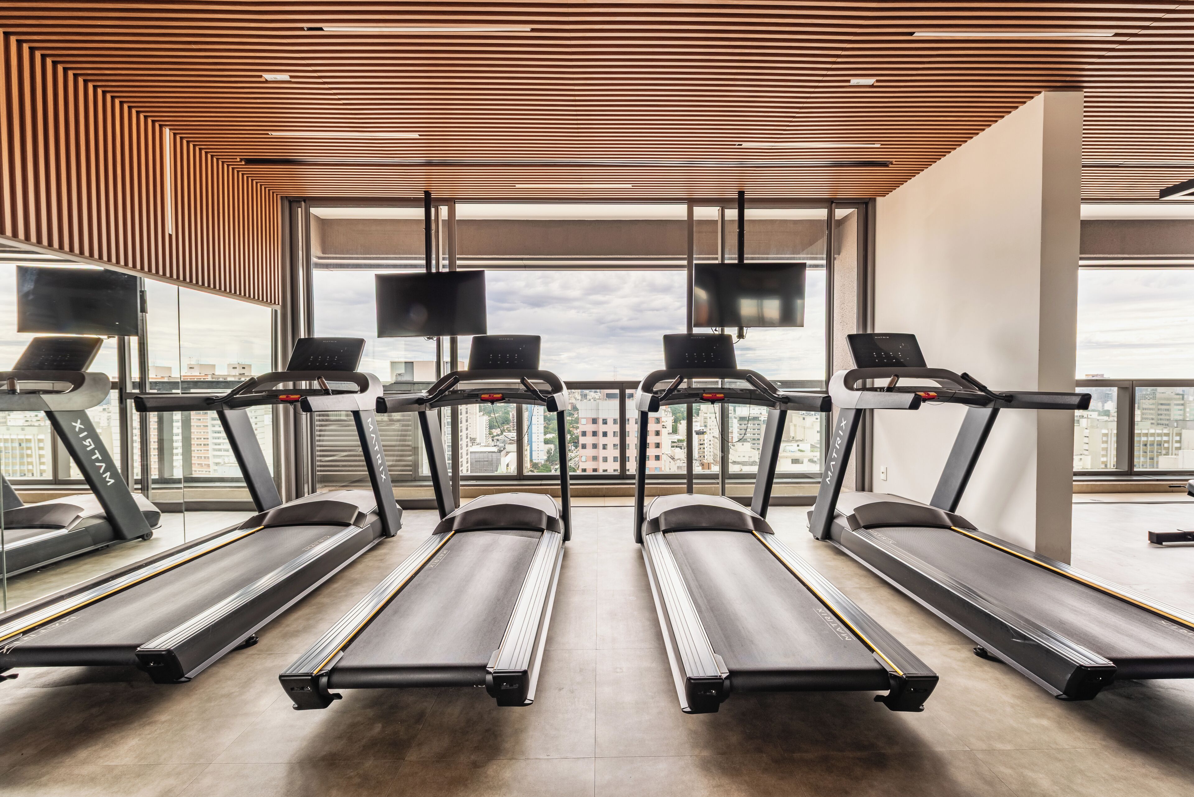 A gym with treadmills, large windows, and a wooden ceiling.