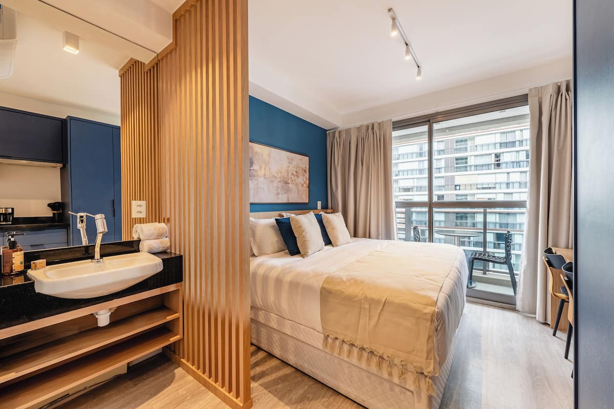A modern hotel room with a large bed, a bathroom with a sink, and a balcony with a view of the city.