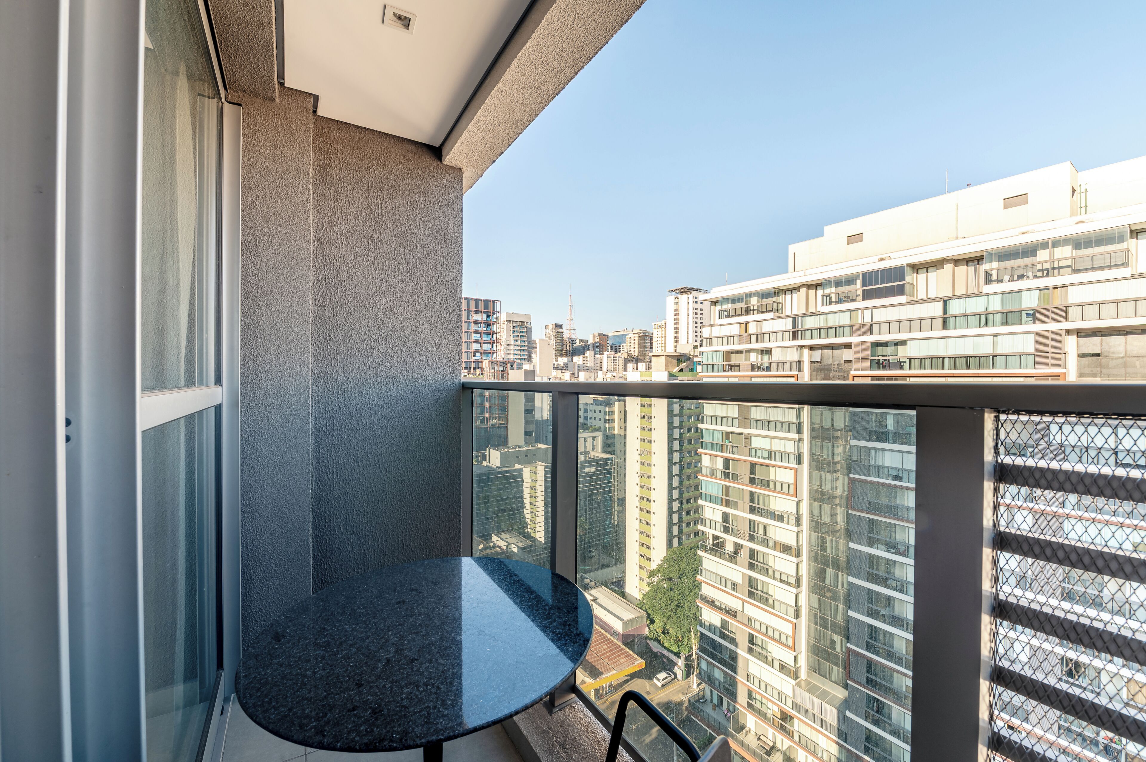 A balcony with a glass door, a round table, and a city view.
