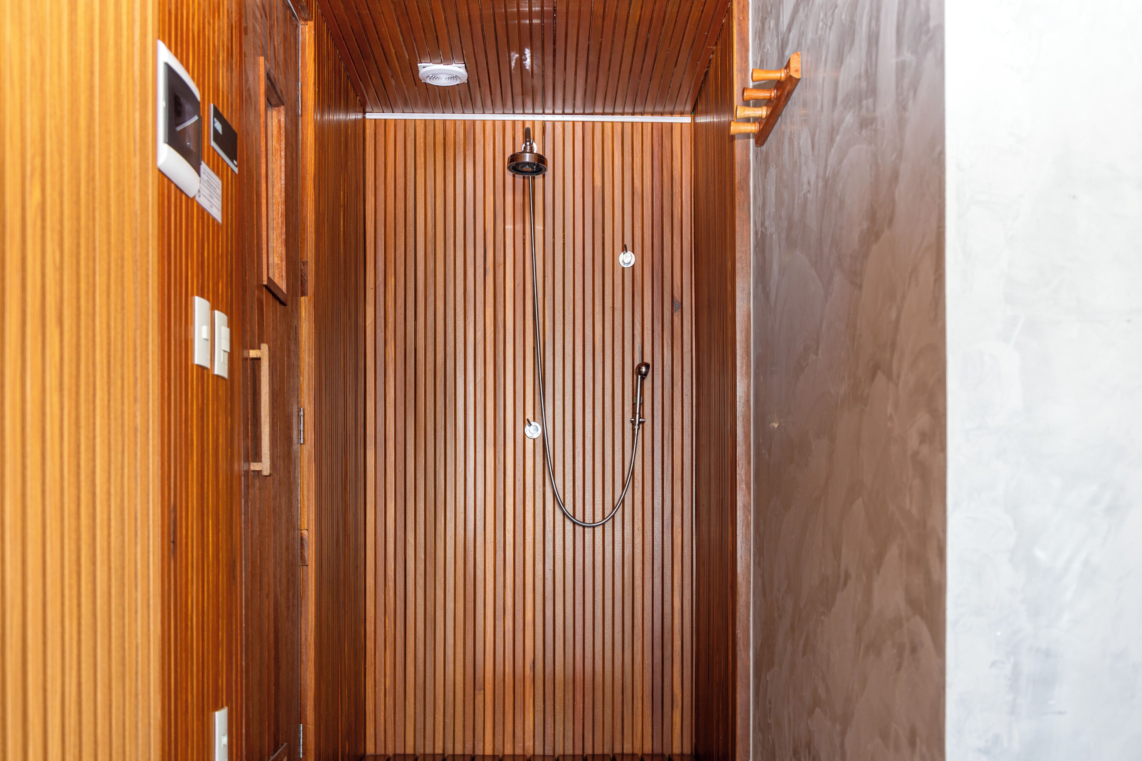 A wooden-paneled shower area with a handheld showerhead and a wall-mounted control panel.