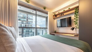 A modern hotel room with a large bed, a TV mounted on the wall, and a view of high-rise buildings. - Movinn Nine - Jardim Paulista (São Paulo)