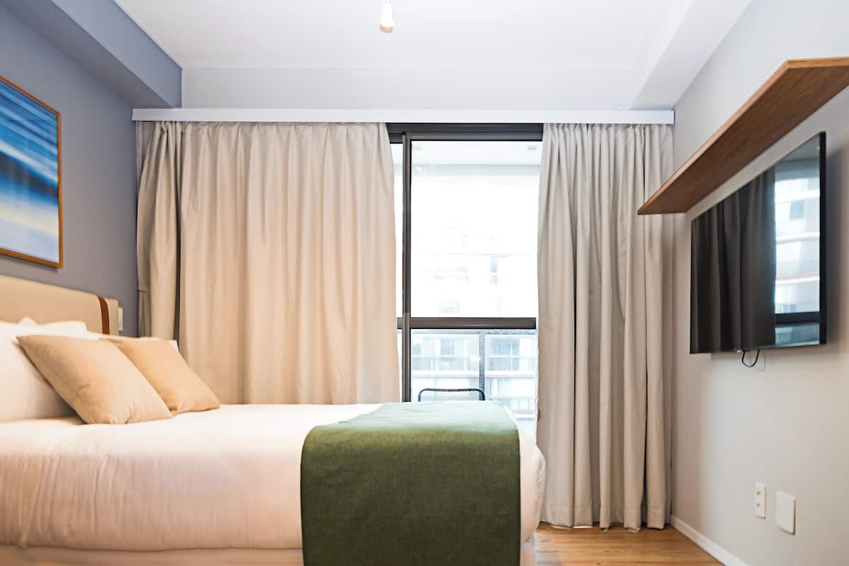A modern hotel room with a bed, curtains, a television, and a window.