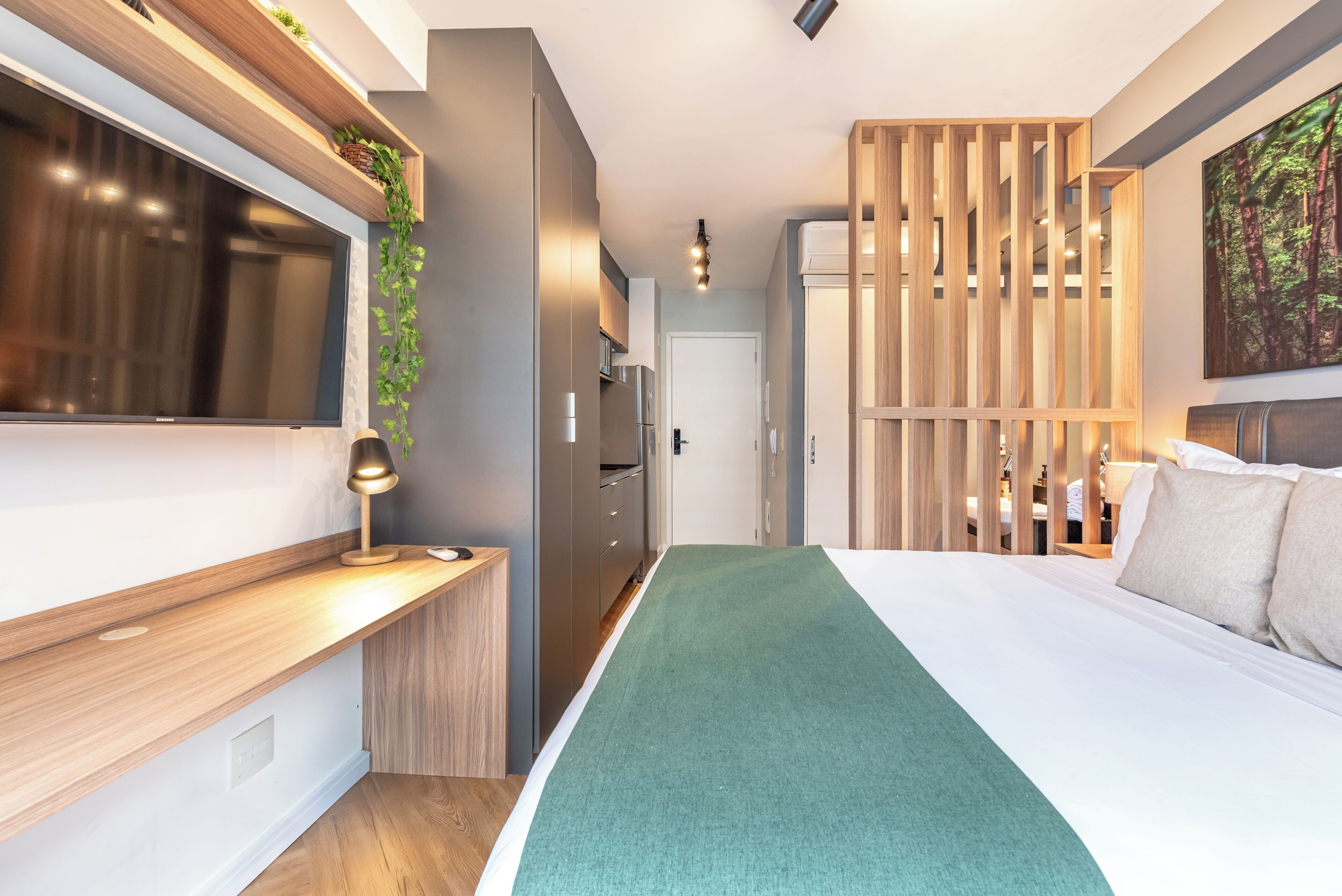 A modern hotel room with a large bed, a desk, a TV, and a wooden partition.