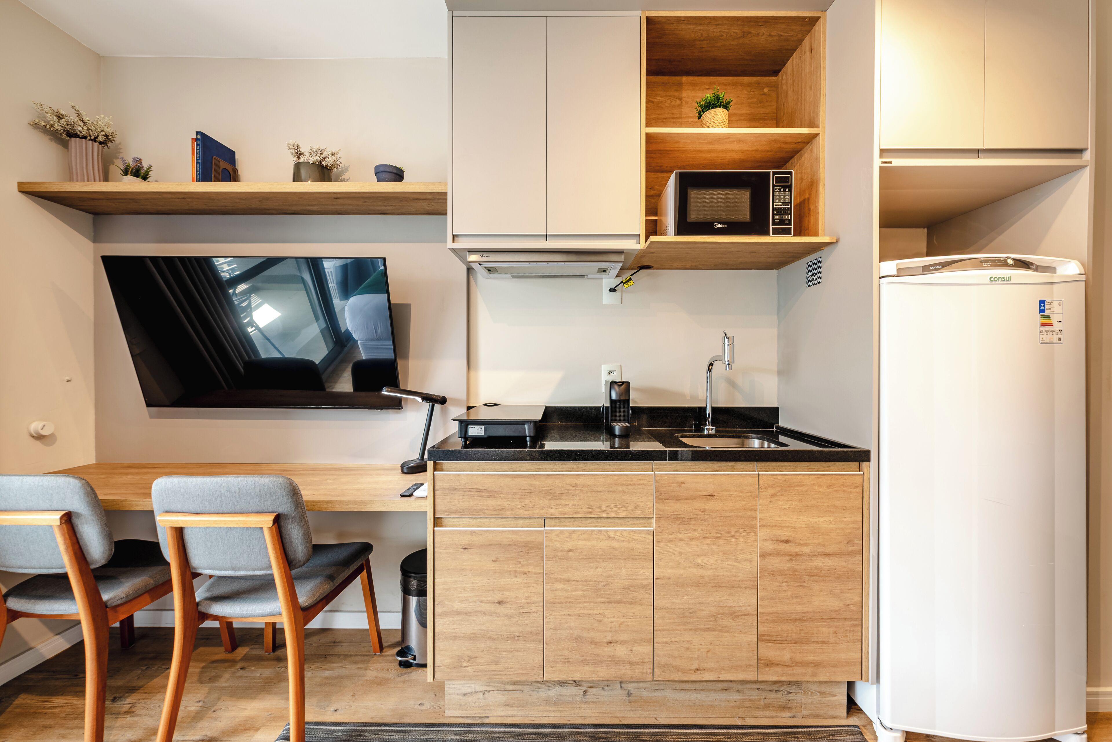 Eine moderne Küche mit integriertem Mikrowellenherd, Spüle und Kühlschrank. Zwei Stühle und ein kleiner Tisch sind ebenfalls vorhanden.