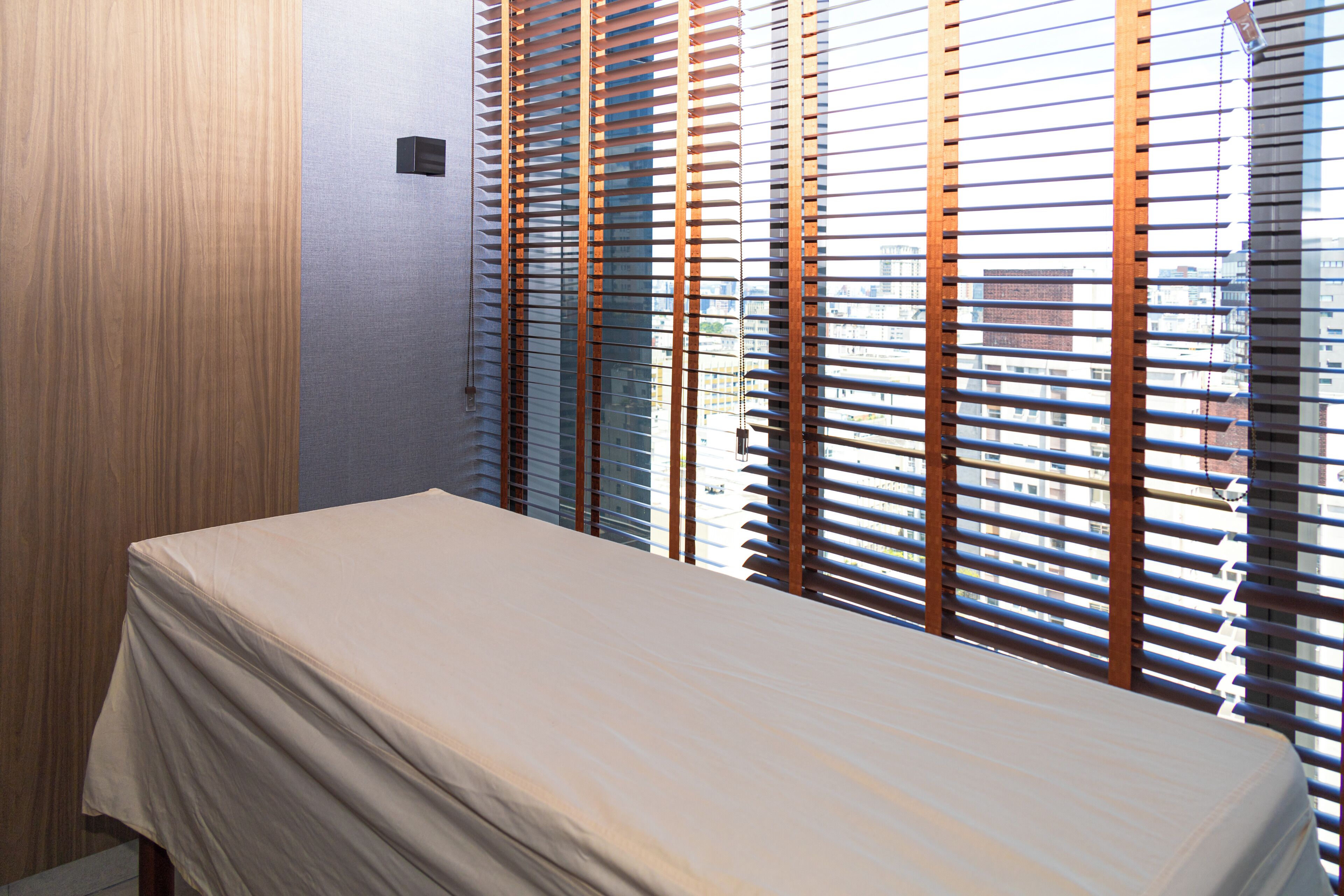 A room with a bed, wooden blinds, and a view of buildings.