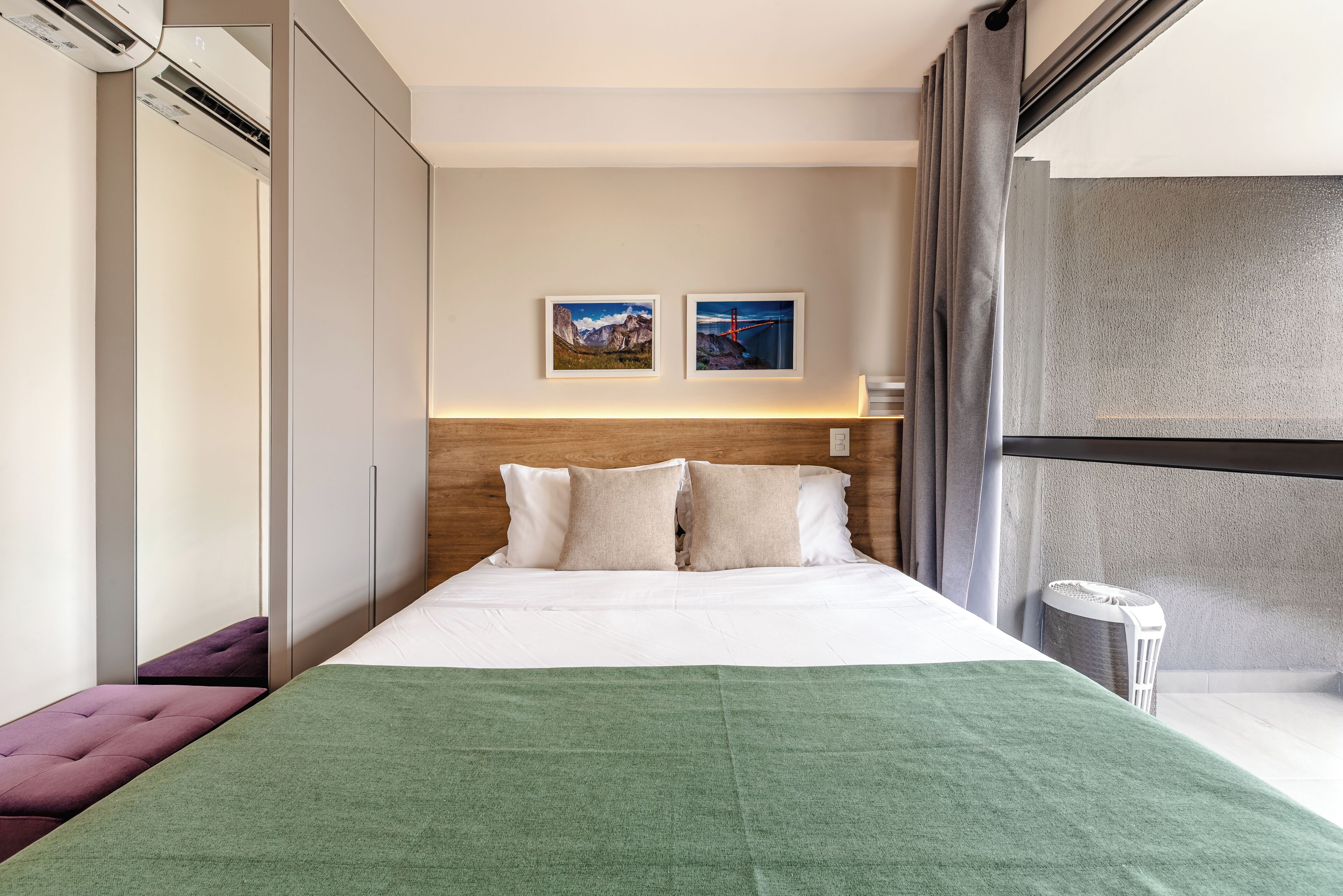 A modern hotel room with a bed, a bench, two framed pictures, a headboard, and a trash bin.