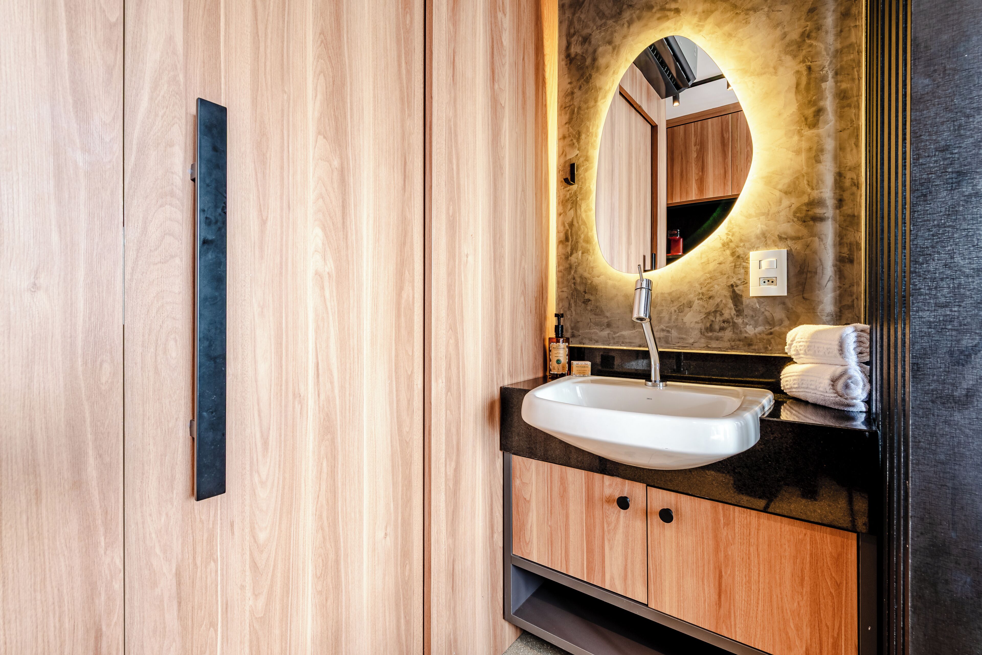 A modern bathroom with a wooden vanity, a white sink, and a mirror with a circular frame.
